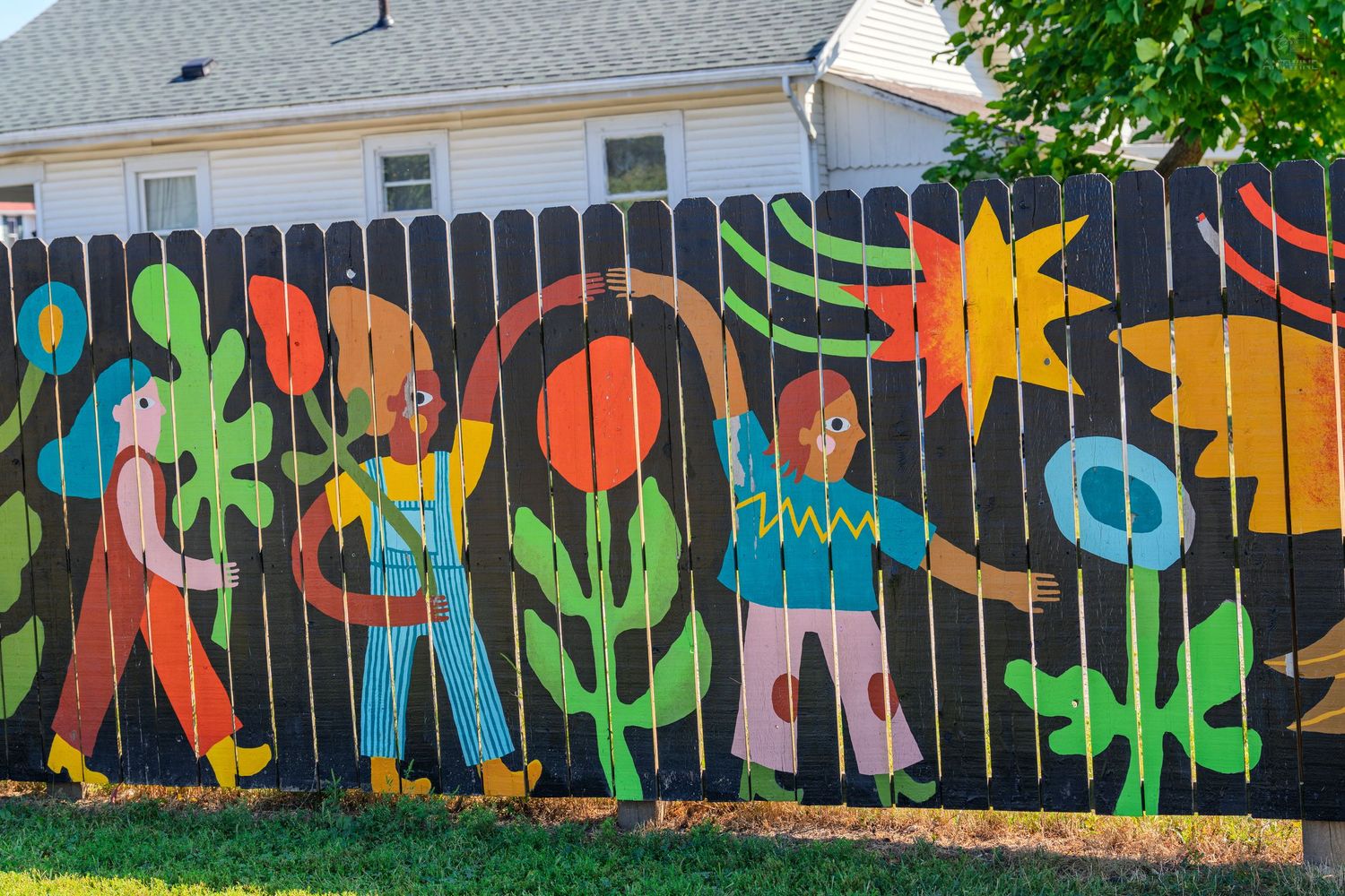 Colorful mural on a wooden fence featuring painted children and flowers in bright, bold colors.