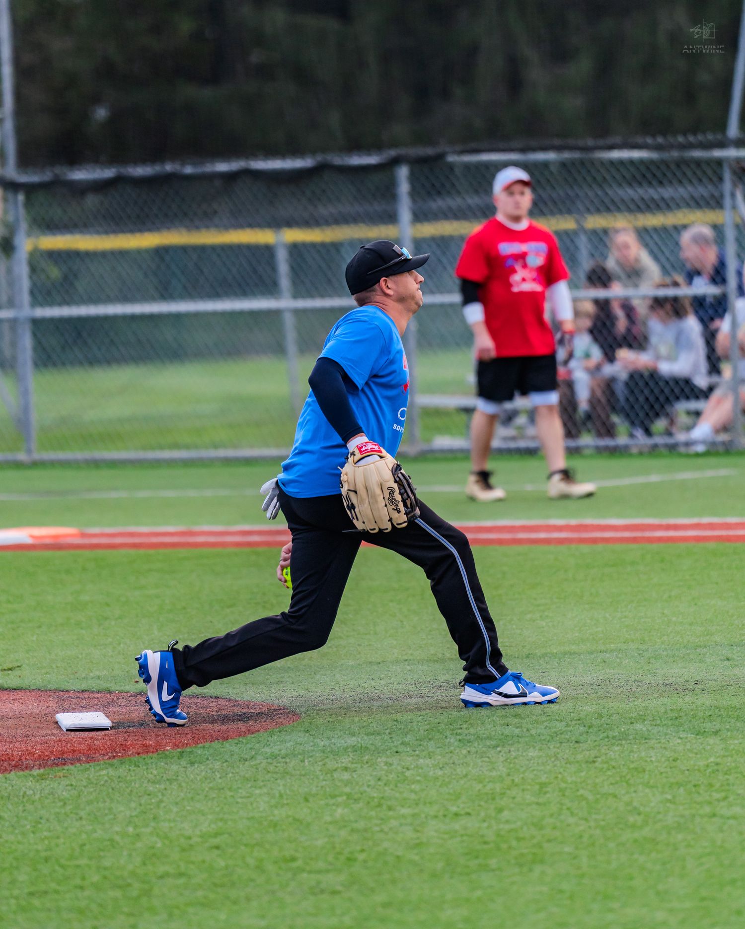 Baseball player in blue jersey fielding a ground ball on the pitcher's mound during a recreational league game.