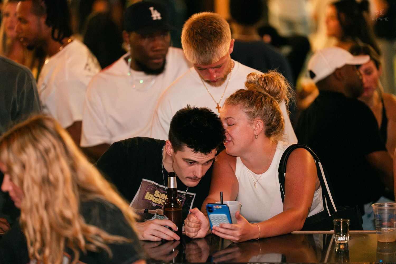 A couple shares a phone screen while sitting at a bar during a social event.
