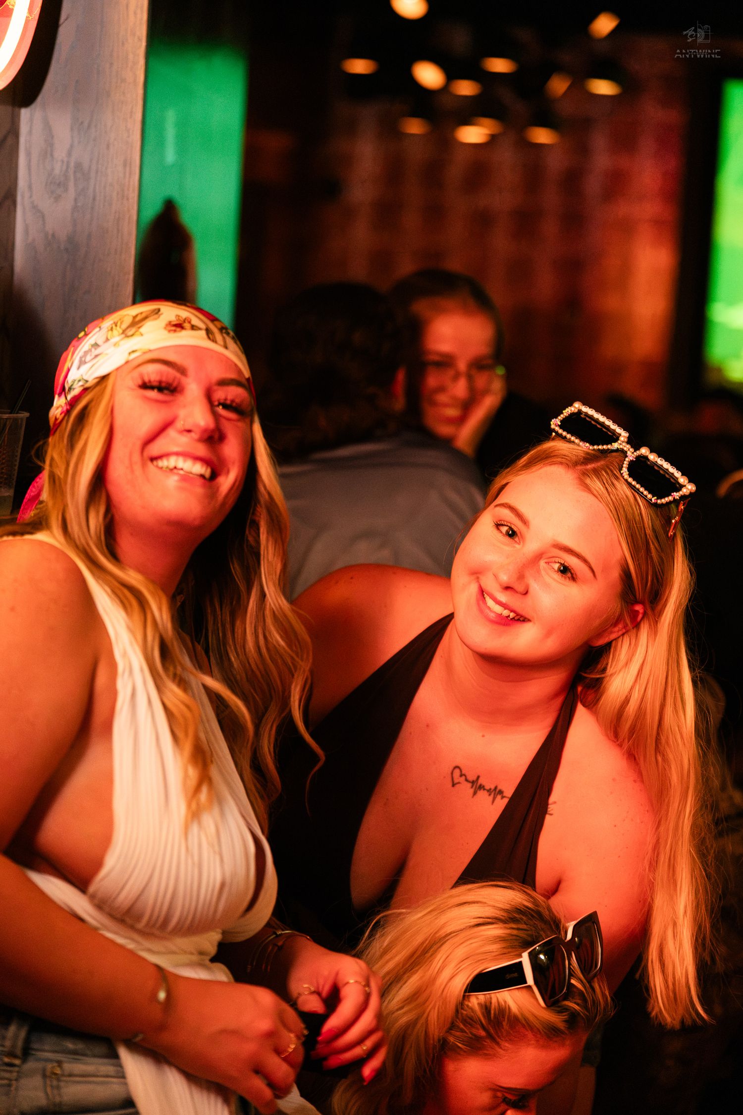 Two smiling young women posing together at a warmly lit nightclub venue.
