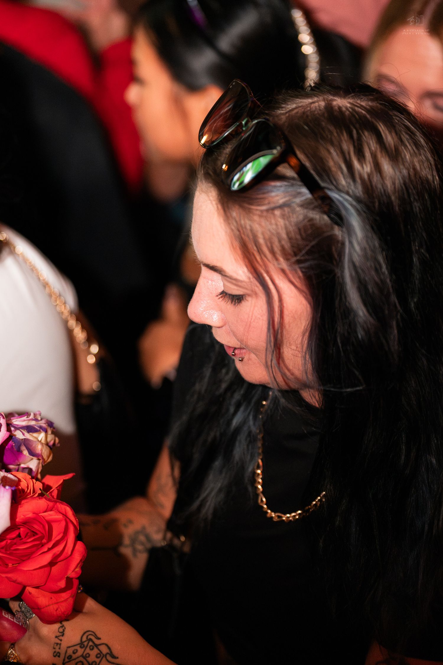 Woman with dark hair and gold chain necklace holding red roses at a party.