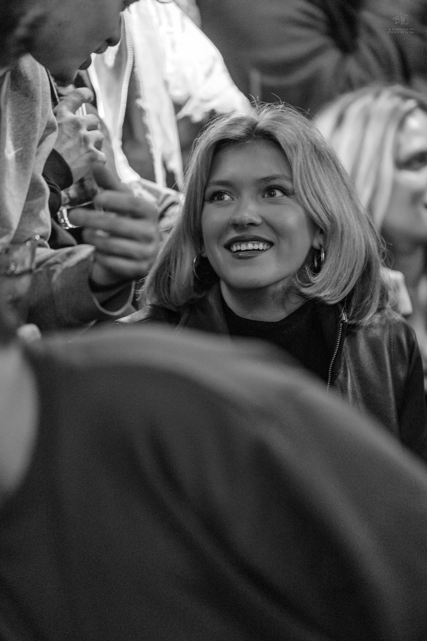 Black and white photo of a joyful blonde woman laughing in a lively crowd.