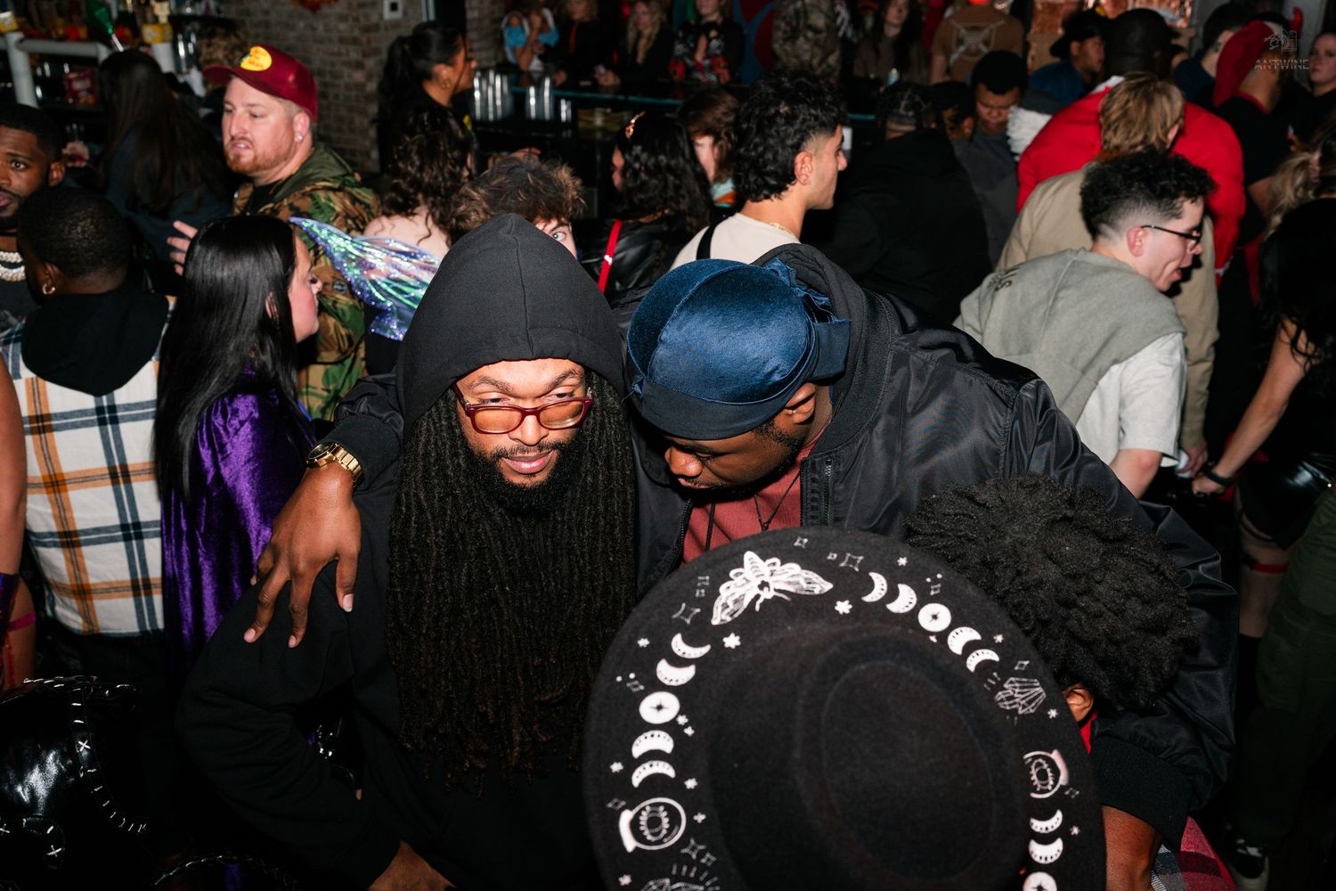 Two men in casual streetwear dancing together at a crowded Halloween party.