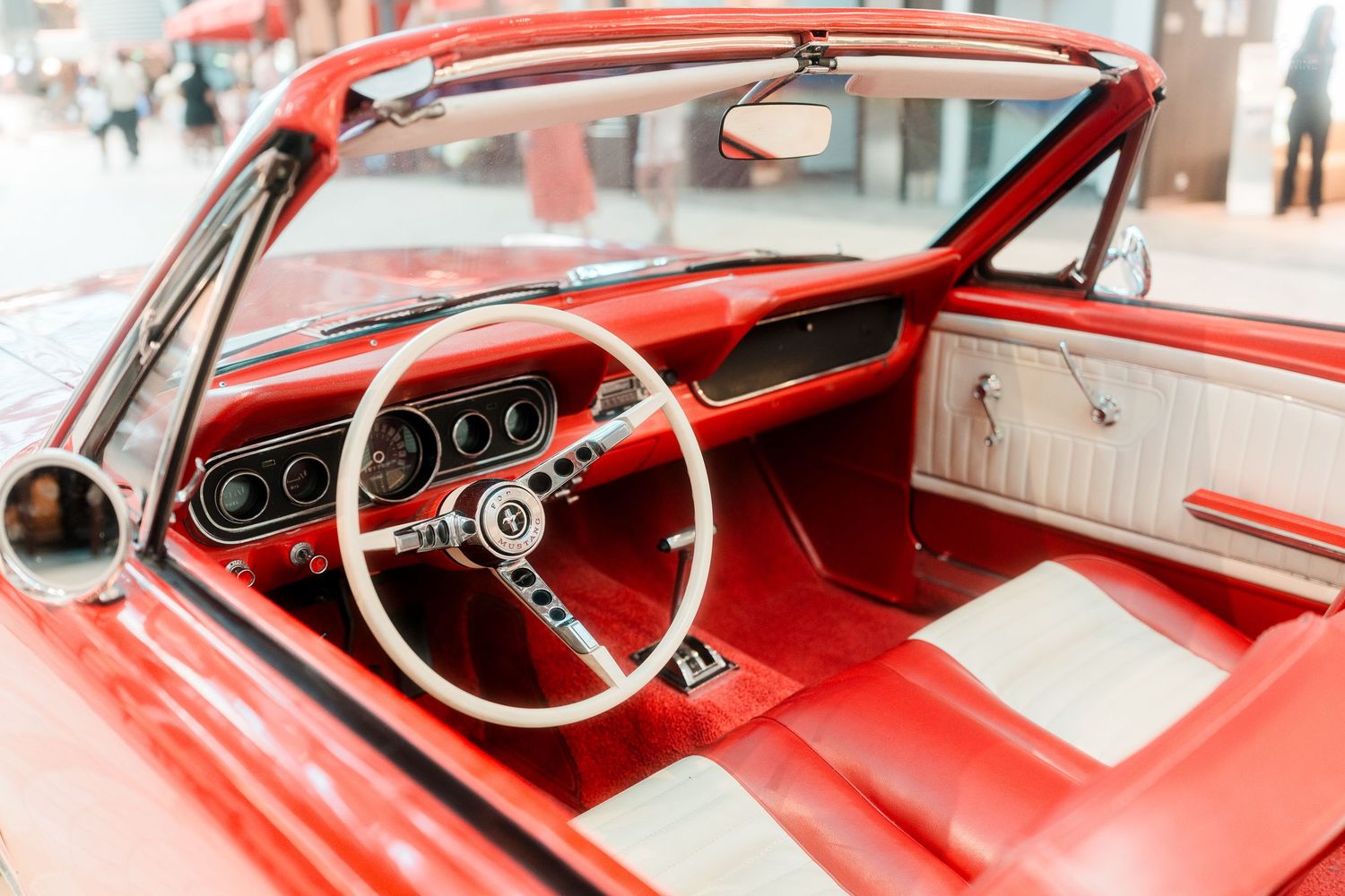 Interior view of a classic red Ford Mustang convertible with white leather seats and vintage dashboard.