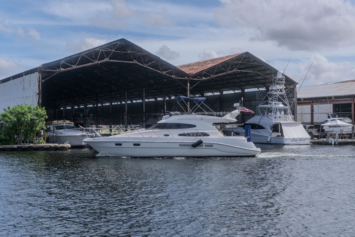 Luxury motor yacht cruising past large covered boat storage facility on a calm waterway.
