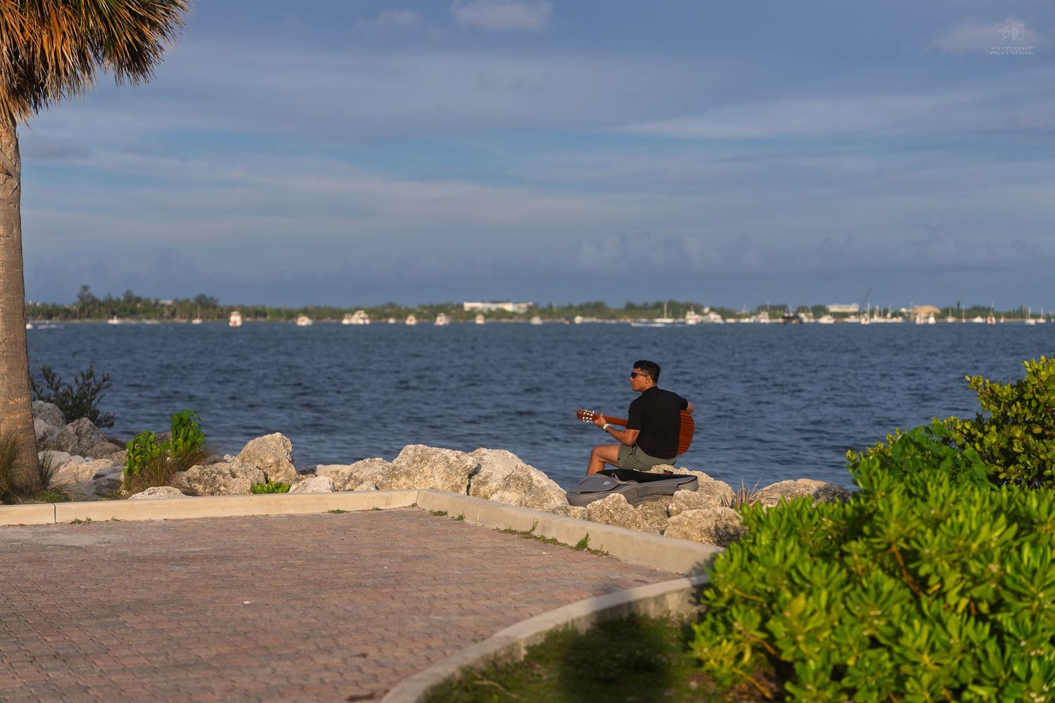 Man sitting on rocks meditating by the calm blue bay waters in Key Biscayne, Florida.