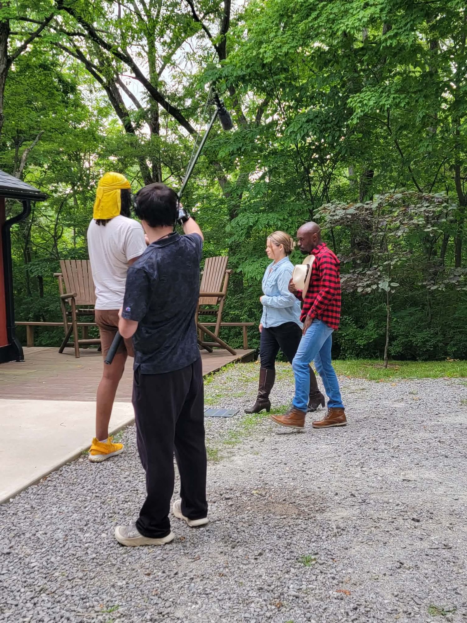 Film crew recording outdoor scene in wooded area with boom mic.