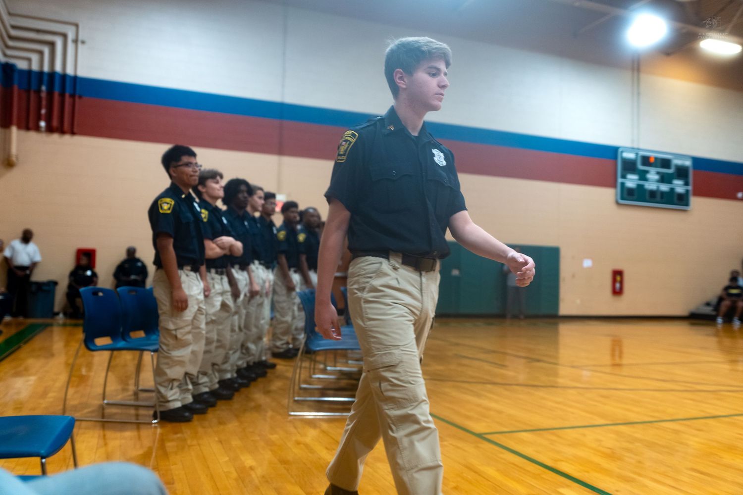 Young cadets in uniform stand in formation inside a school gymnasium during a law enforcement youth program.