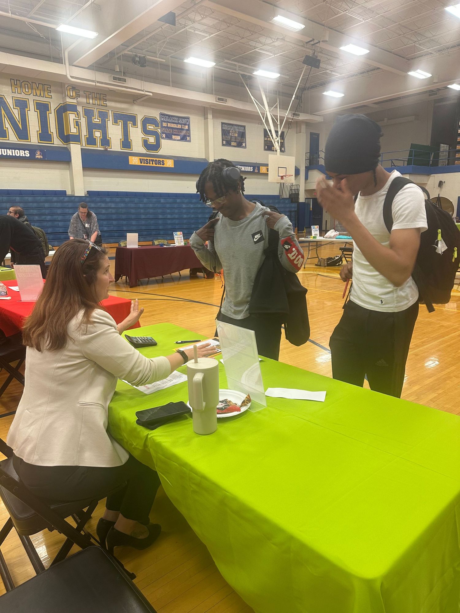 Students meet with a recruiter at a green table during a career fair in a high school gymnasium.
