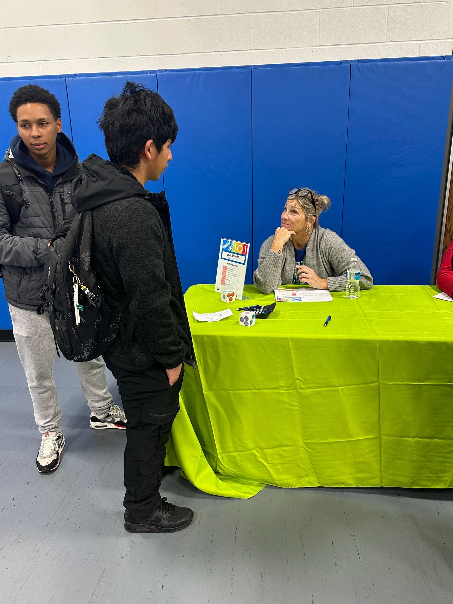 Two students speak with a representative seated at a green table at an indoor career fair.
