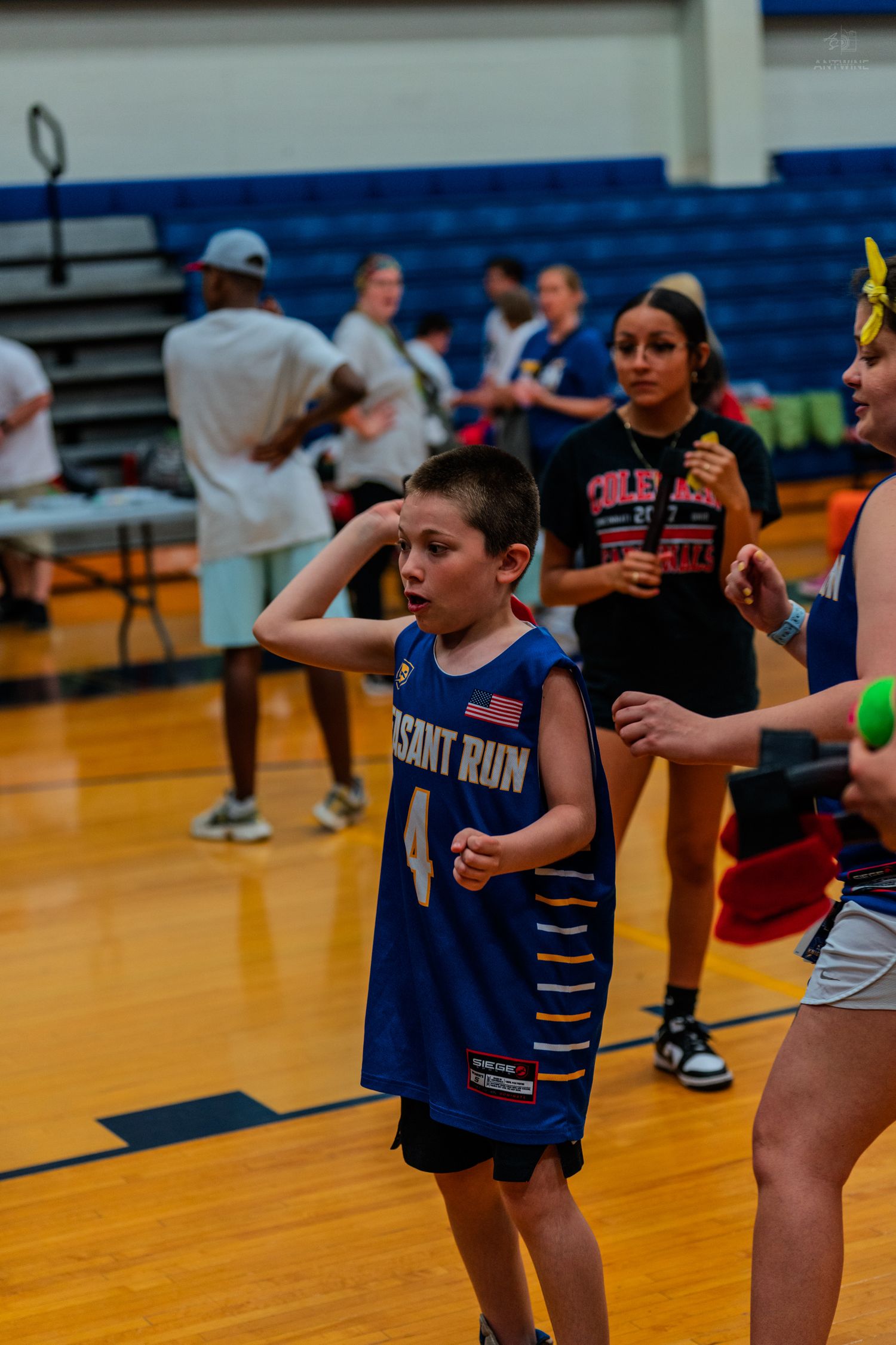 Young boy in blue Pleasant Run basketball jersey #4 saluting on indoor court during youth sports event.