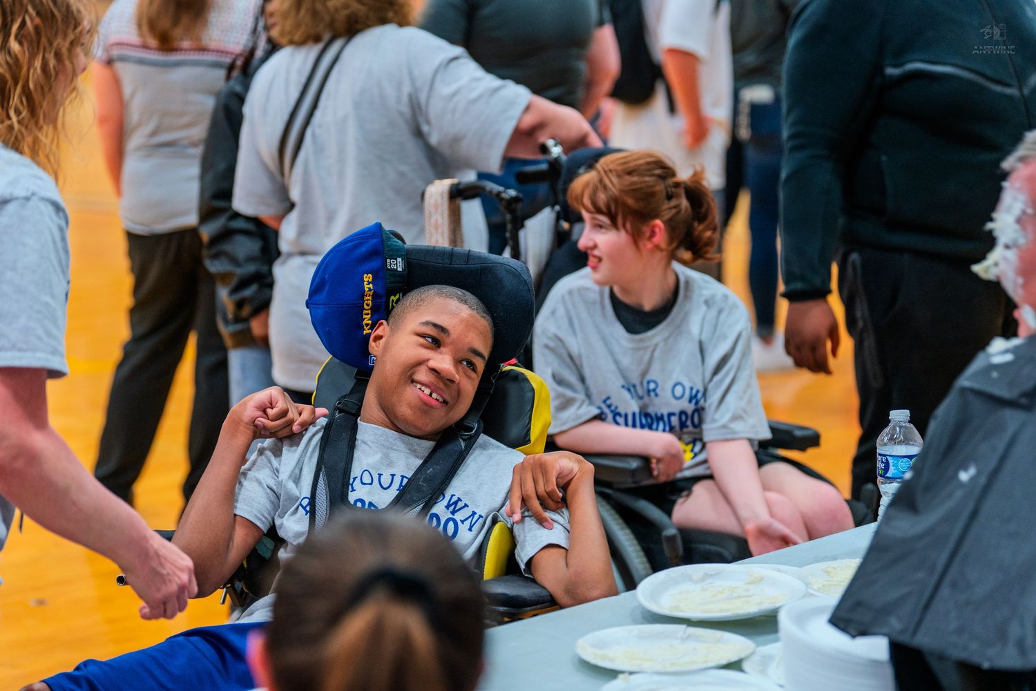 Children with disabilities smile and laugh together at an inclusive community event, one seated in a wheelchair.