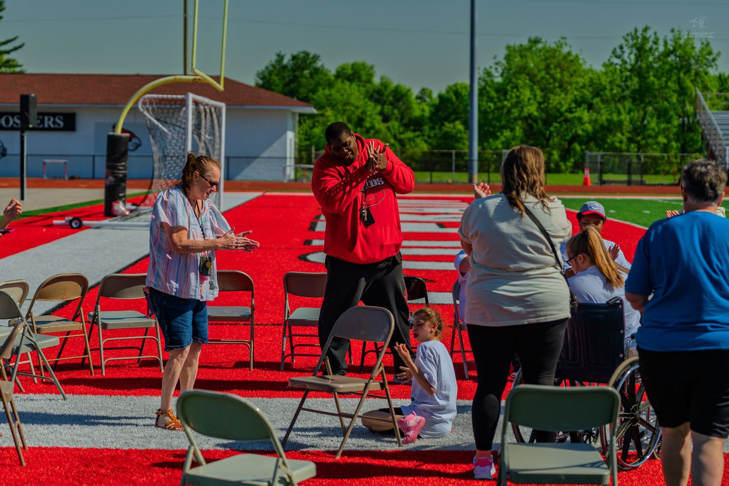 People gather on a red track at an outdoor stadium during a graduation ceremony on a sunny day.