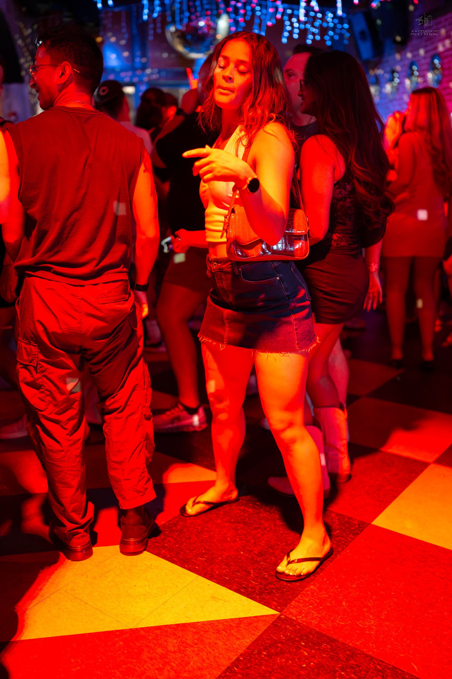 People dancing on a checkered floor under red and blue lights in a vibrant nightclub setting.