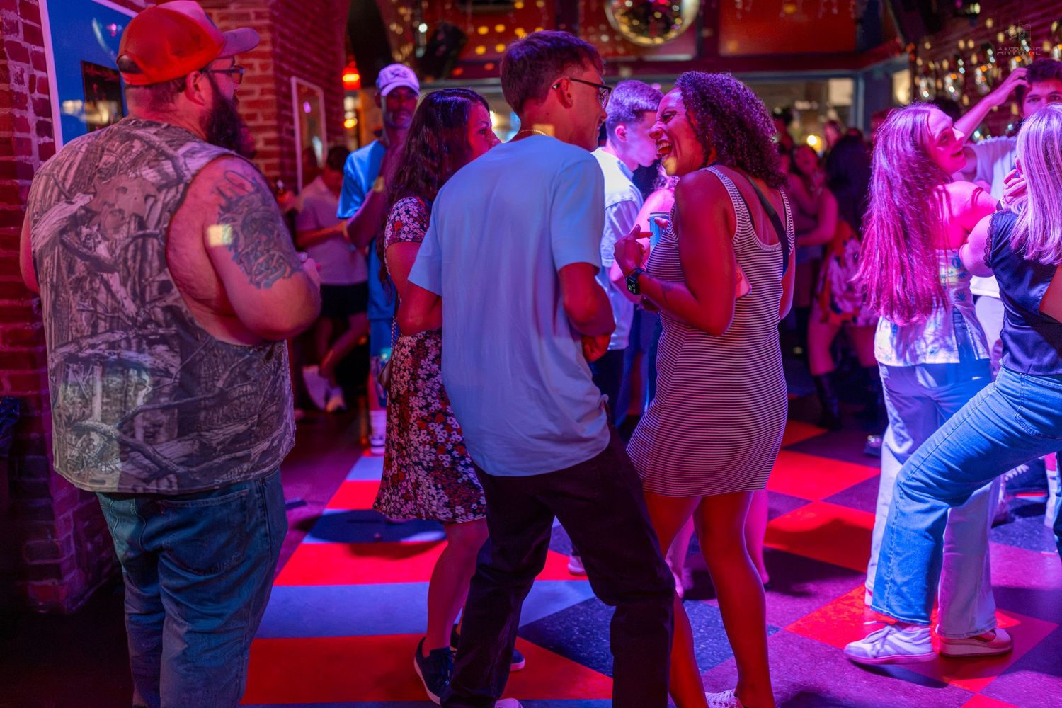Couples dancing at a lively bar with red neon lights and a festive atmosphere.