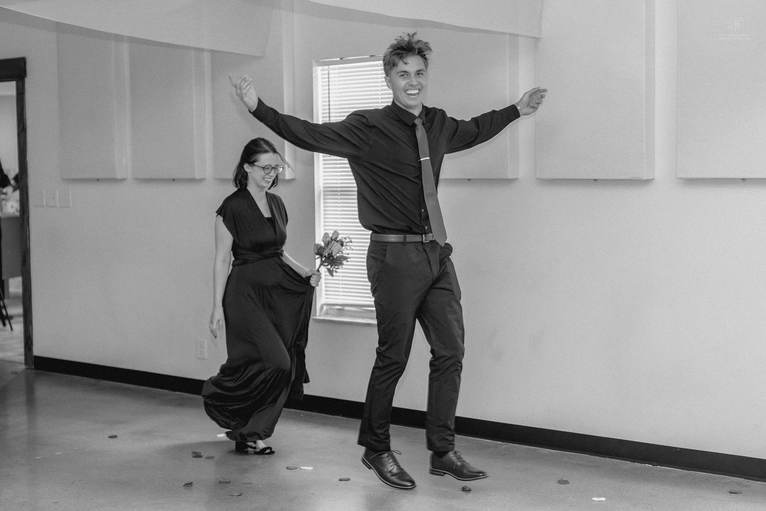 Joyful couple dances energetically in black and white photo during wedding reception celebration.