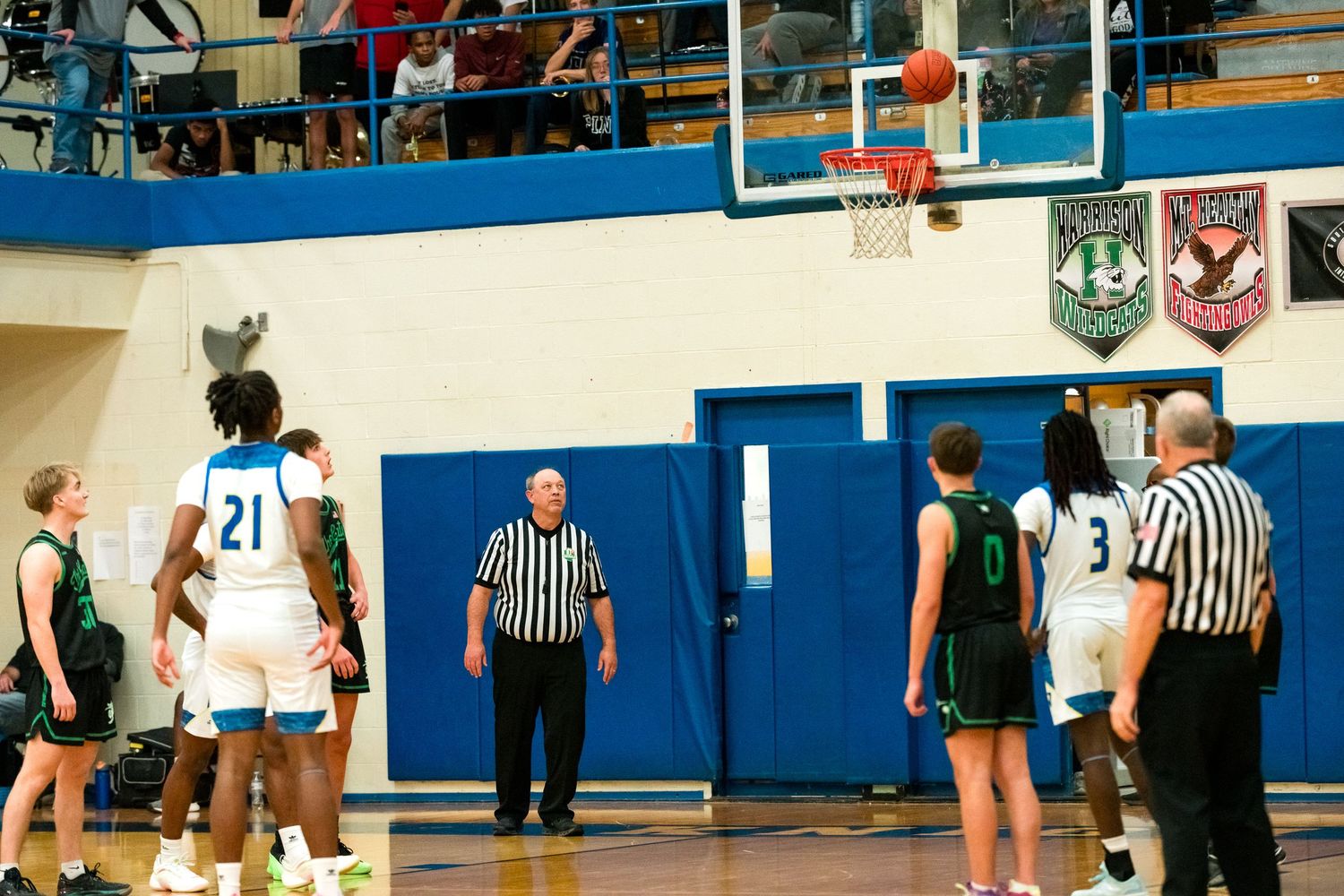 High school basketball game with player number 21 shooting a free throw while referees and players line up.