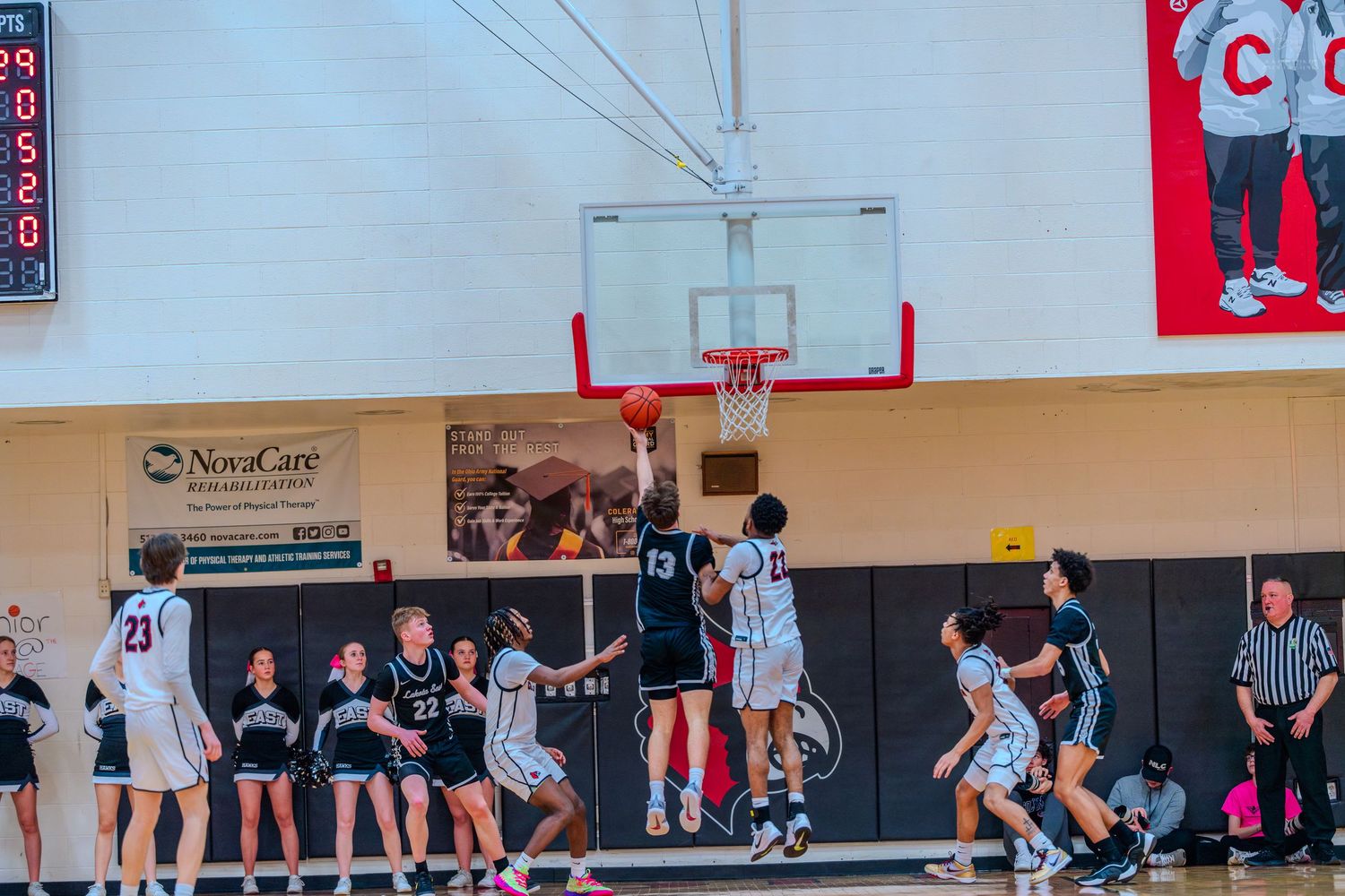 High school basketball player #13 in black uniform attempts a layup during an indoor gymnasium game.