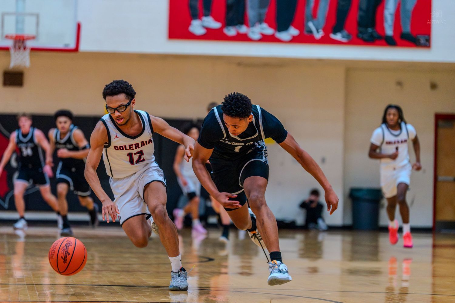 Two basketball players race for a loose ball during a competitive high school basketball game.