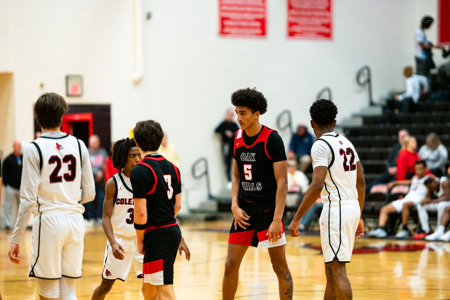 Basketball players from opposing teams walk across the court during a high school basketball game.