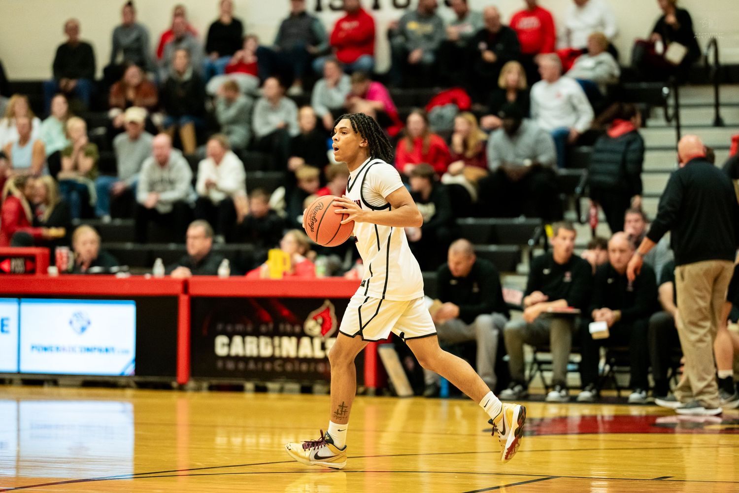 High school basketball player in white Colerain uniform dribbles ball during well-attended game.