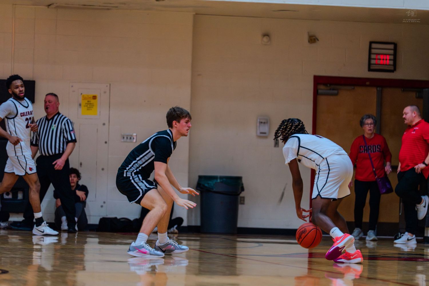 Two high school basketball players face off in defensive dribble challenge during indoor gymnasium game.