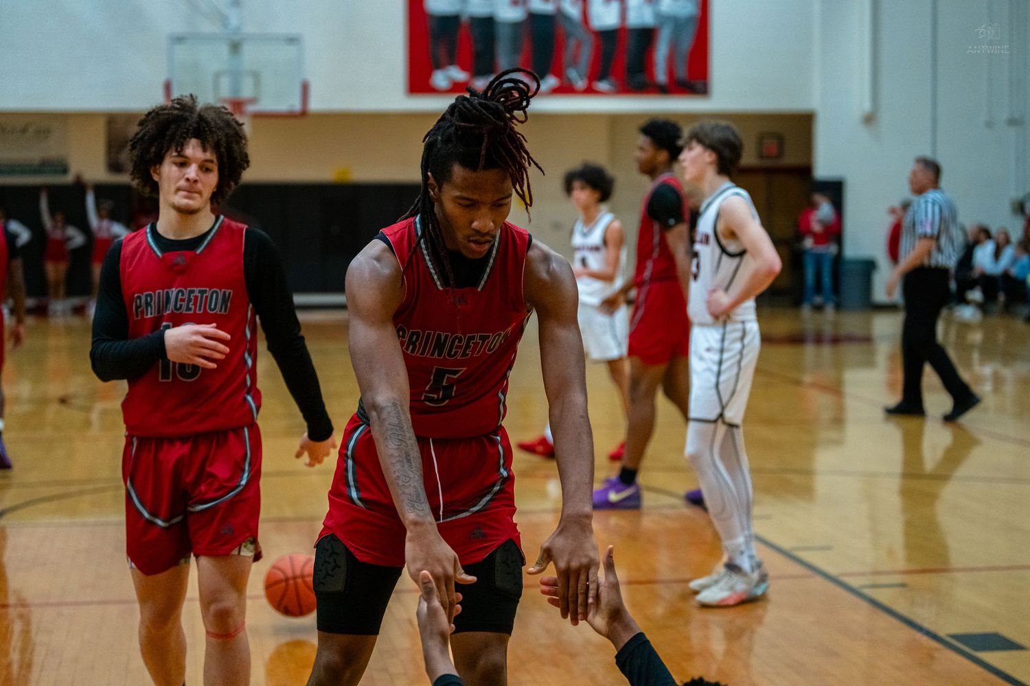 High school basketball players in red uniforms walk across the court during a game timeout.