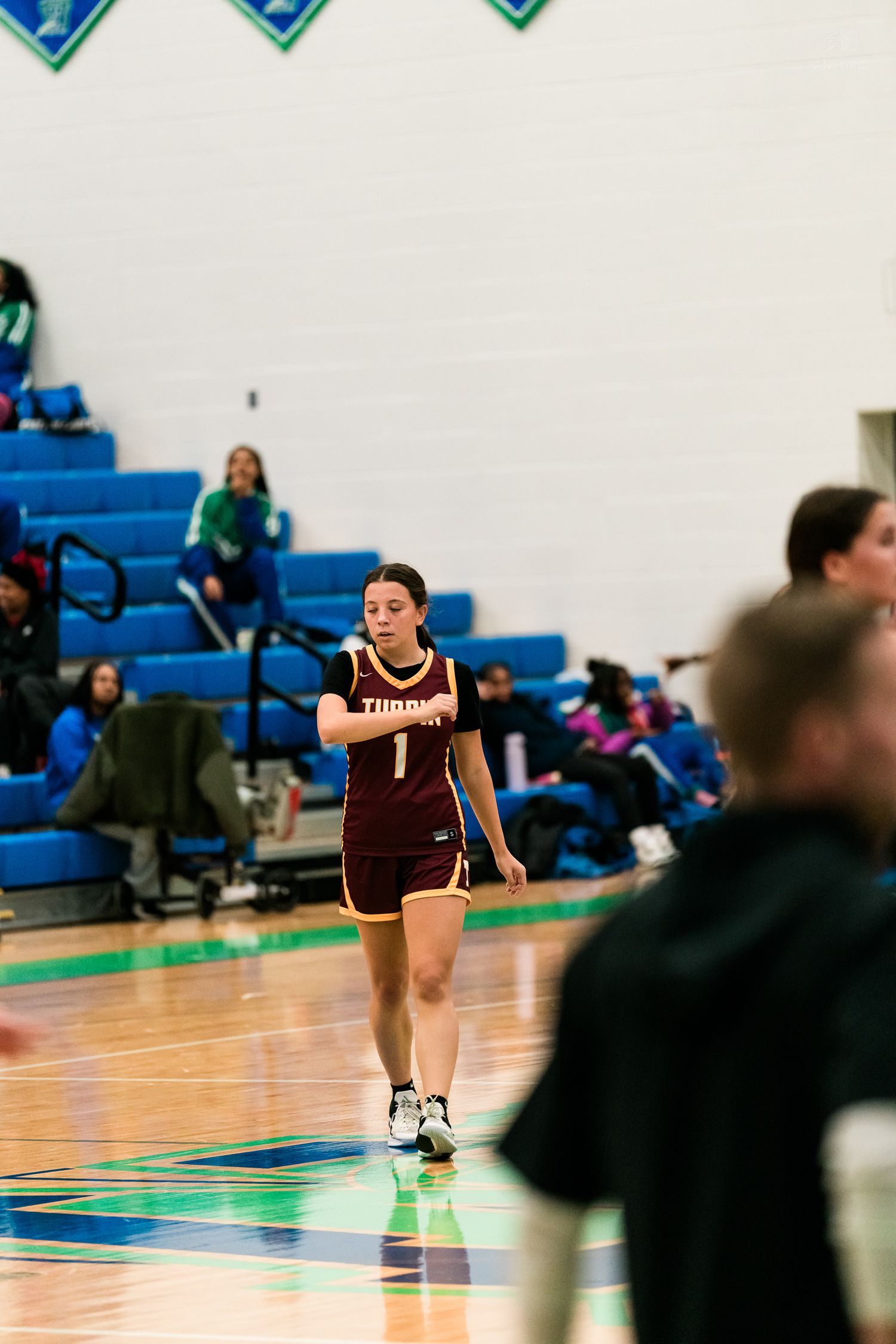 A female basketball player wearing maroon number 1 jersey walks on the court during a girls basketball game.