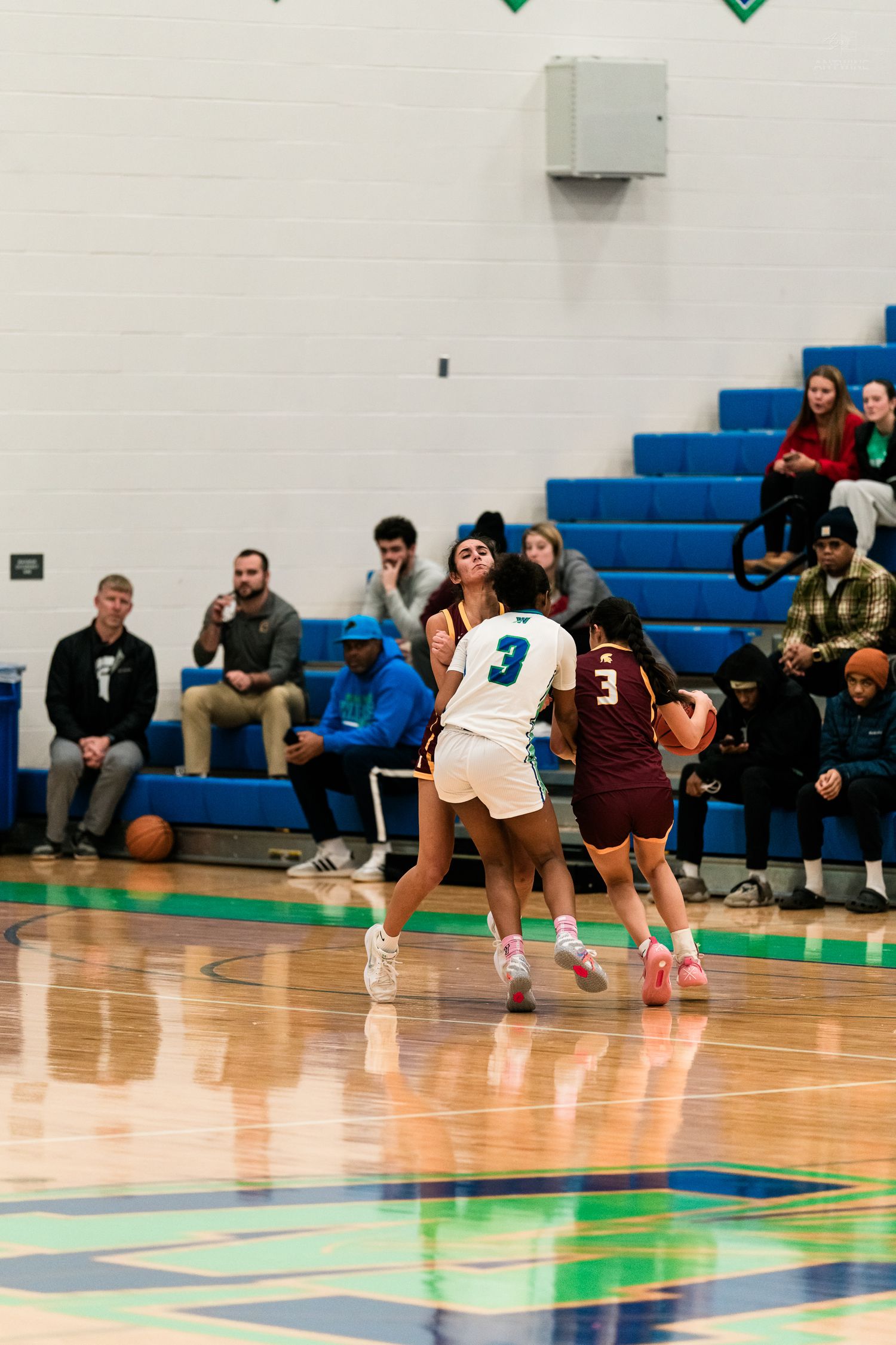 Two female basketball players in white and maroon uniforms compete during a high school girls basketball game in a blue gymnasium.