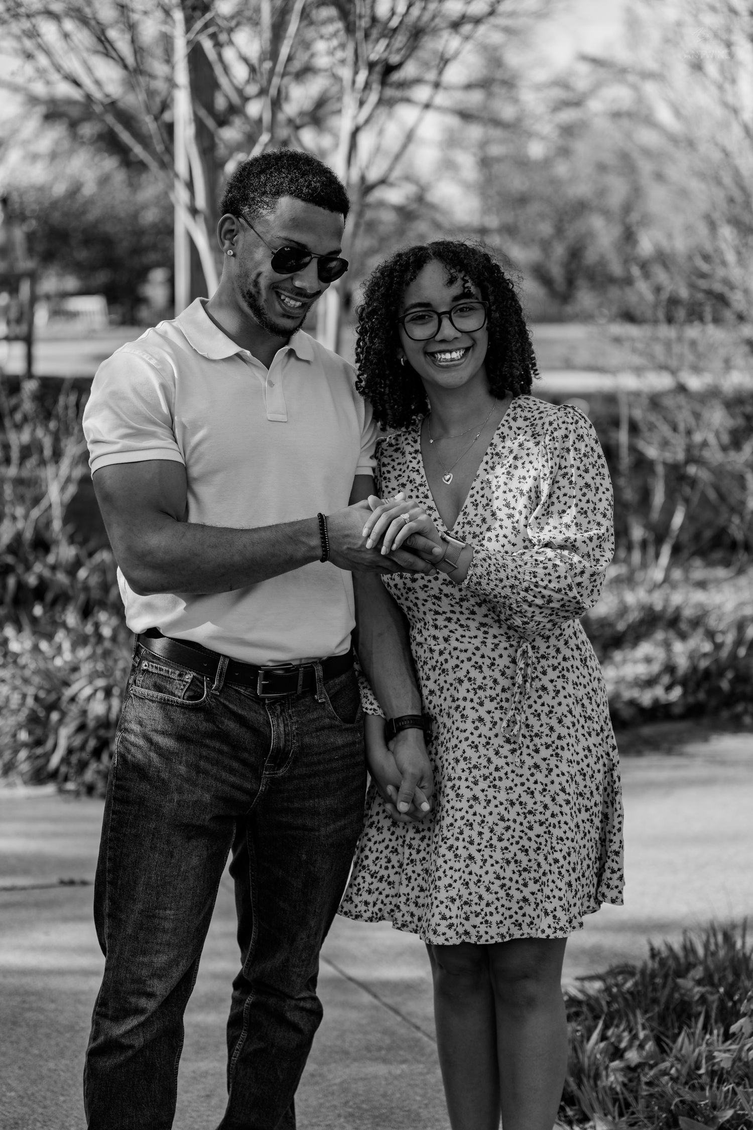 Black and white portrait of a happy couple holding hands and smiling together in an outdoor park setting.