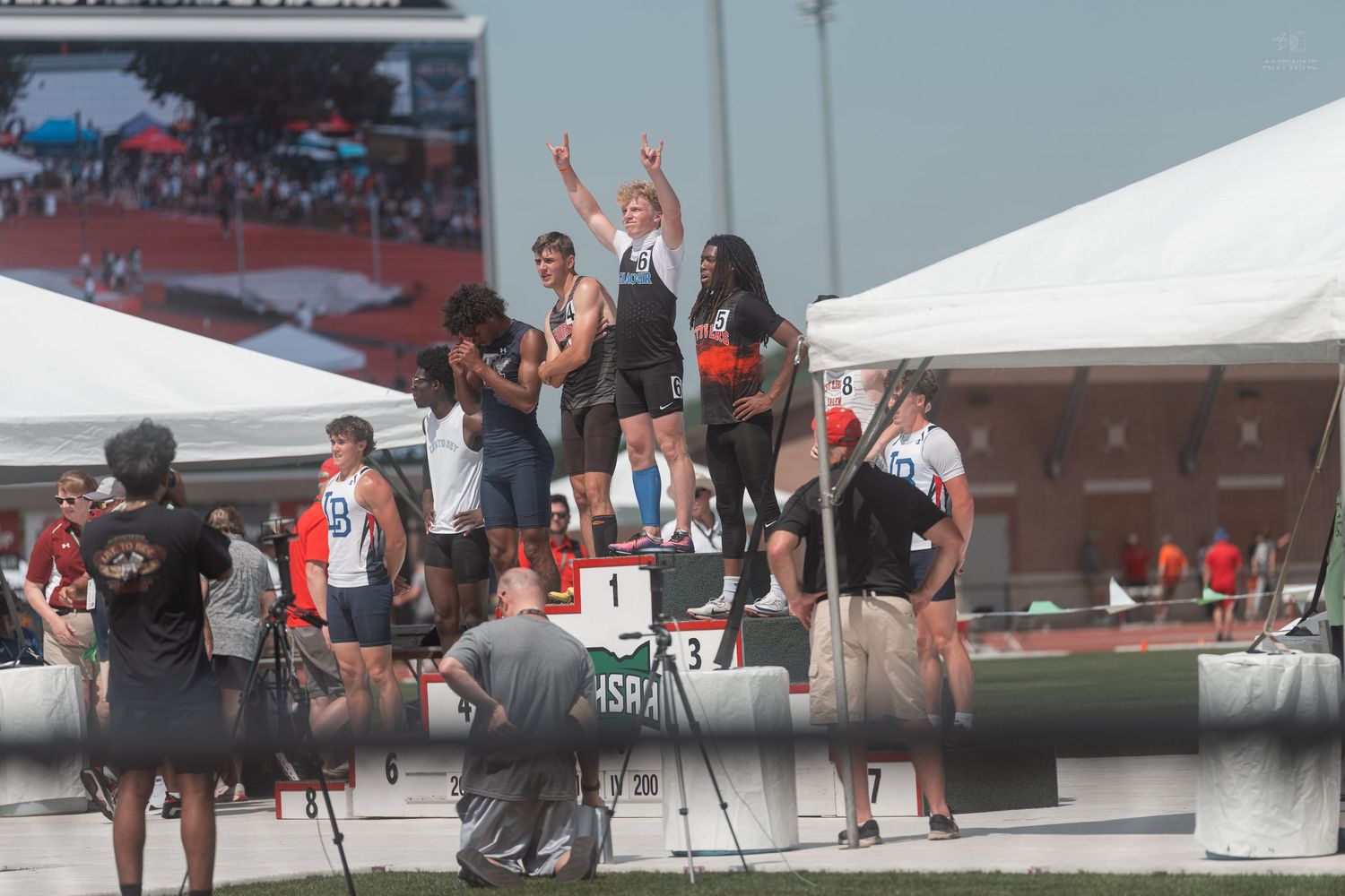 Male athletes raise their arms in victory on the winners podium at an outdoor track and field competition.