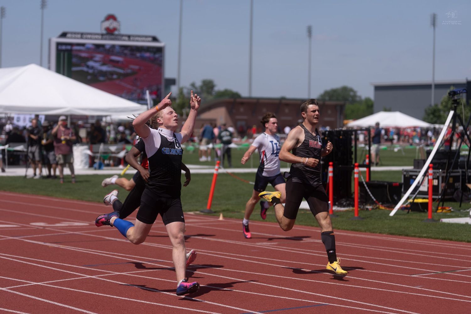 Athlete celebrates crossing the finish line with arms raised at an outdoor track championship meet.