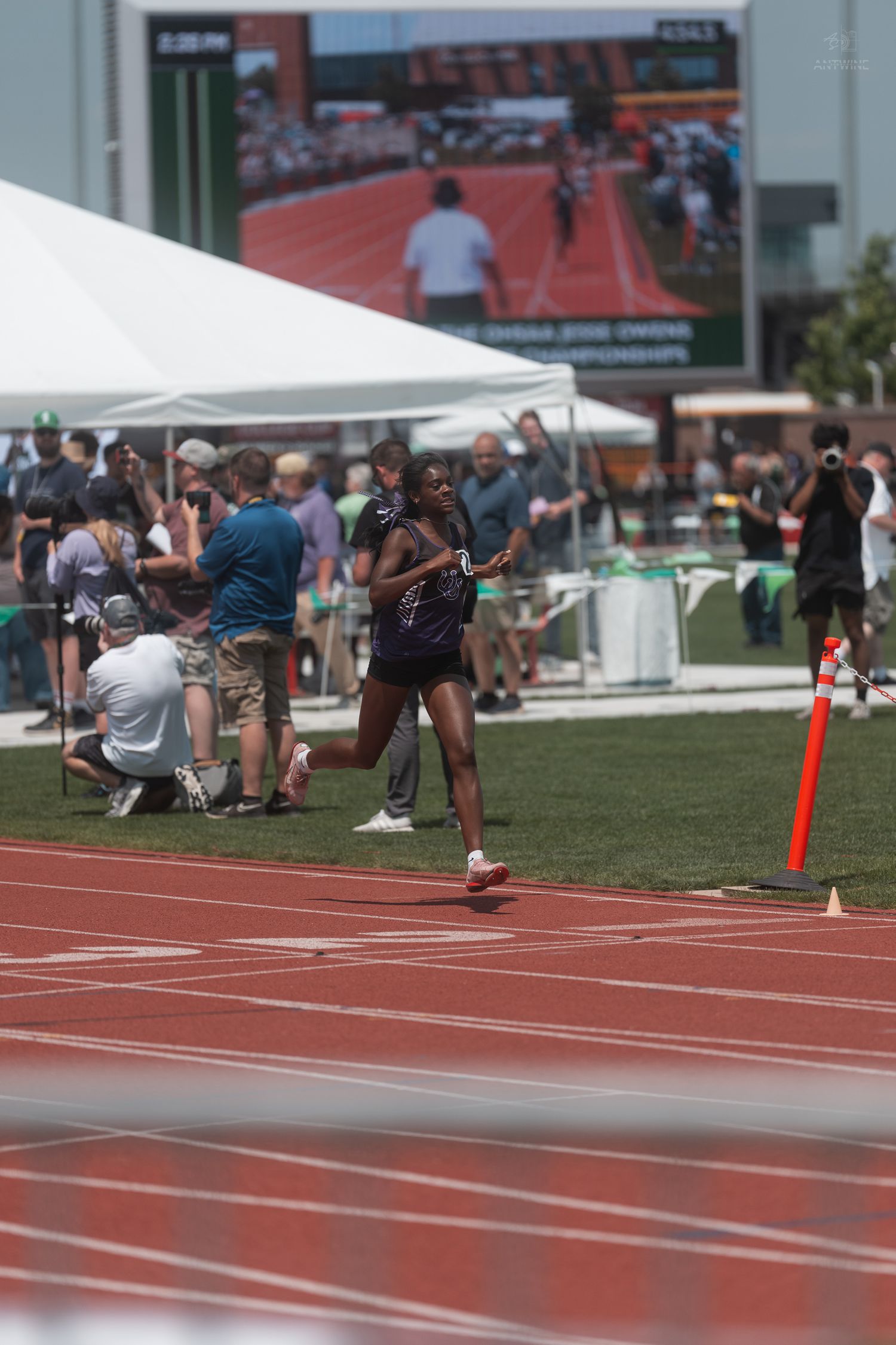 Black female athlete runs solo on a red track at Jesse Owens Memorial Stadium during a championship track meet.