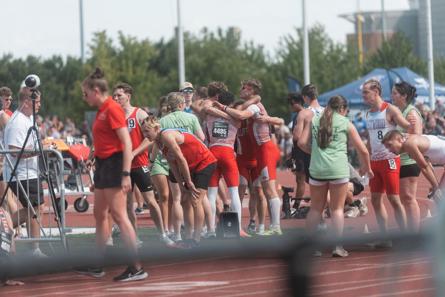 Athletes in red and green uniforms huddle together on a track field during a competitive meet.