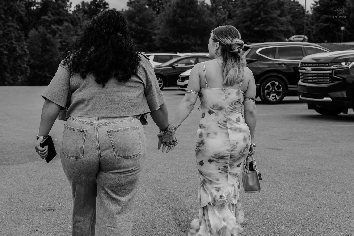 Black and white photo of two women holding hands walking through a parking lot.