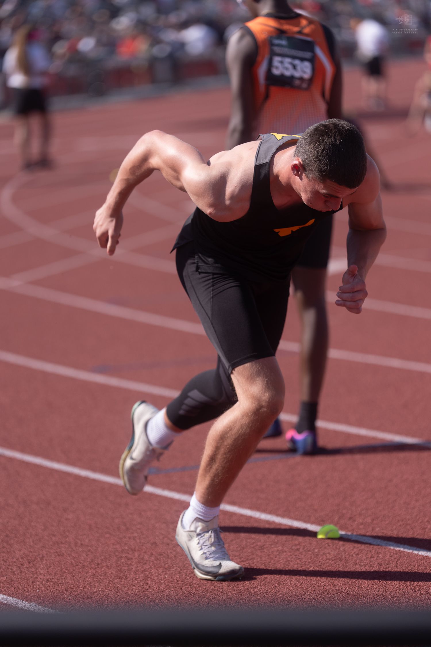 Male sprinter in black uniform explodes out of starting blocks during competitive track and field event.