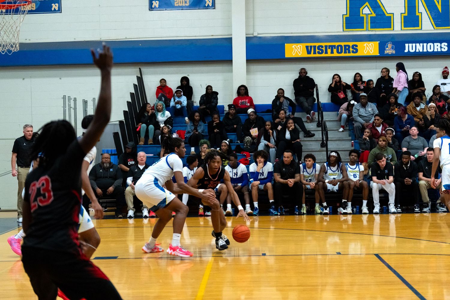High school basketball player in white dribbles the ball during a game with crowd watching courtside.