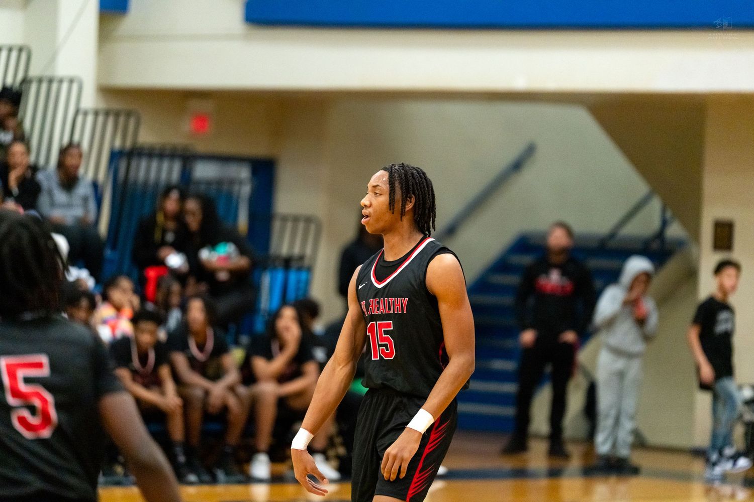 A player wearing jersey number 15 in black looks up during a high school basketball game with fans watching.