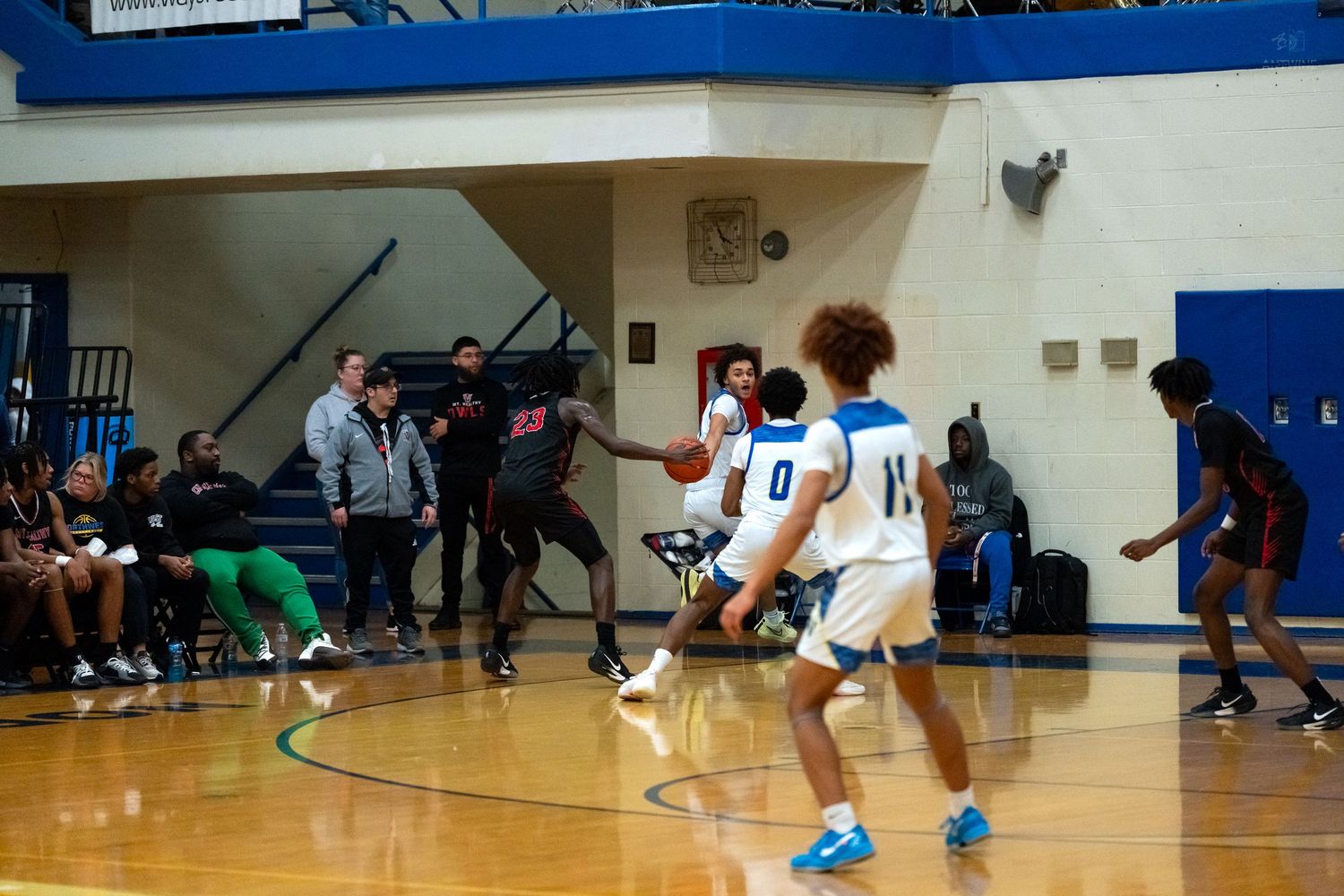 High school basketball players in white uniforms execute a play near the three-point line during a game.