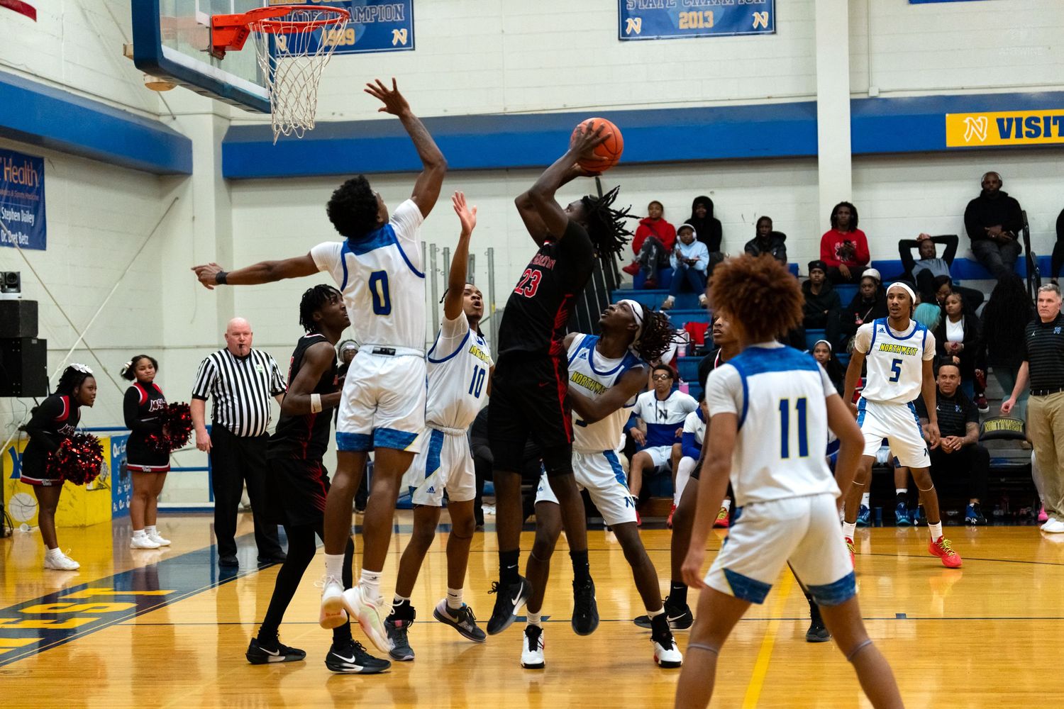 Basketball player in red uniform attempts a shot over multiple defenders during a high school game.