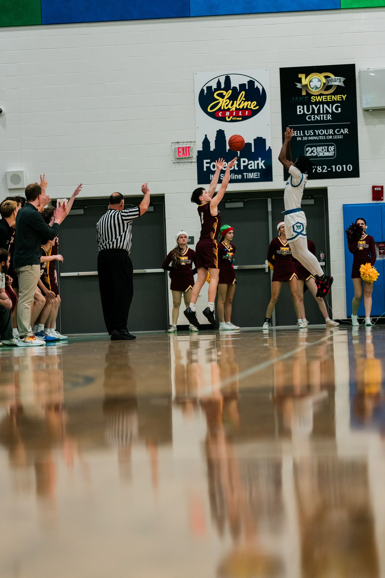 High school basketball player attempts a shot near the baseline as referee and cheerleaders watch nearby.
