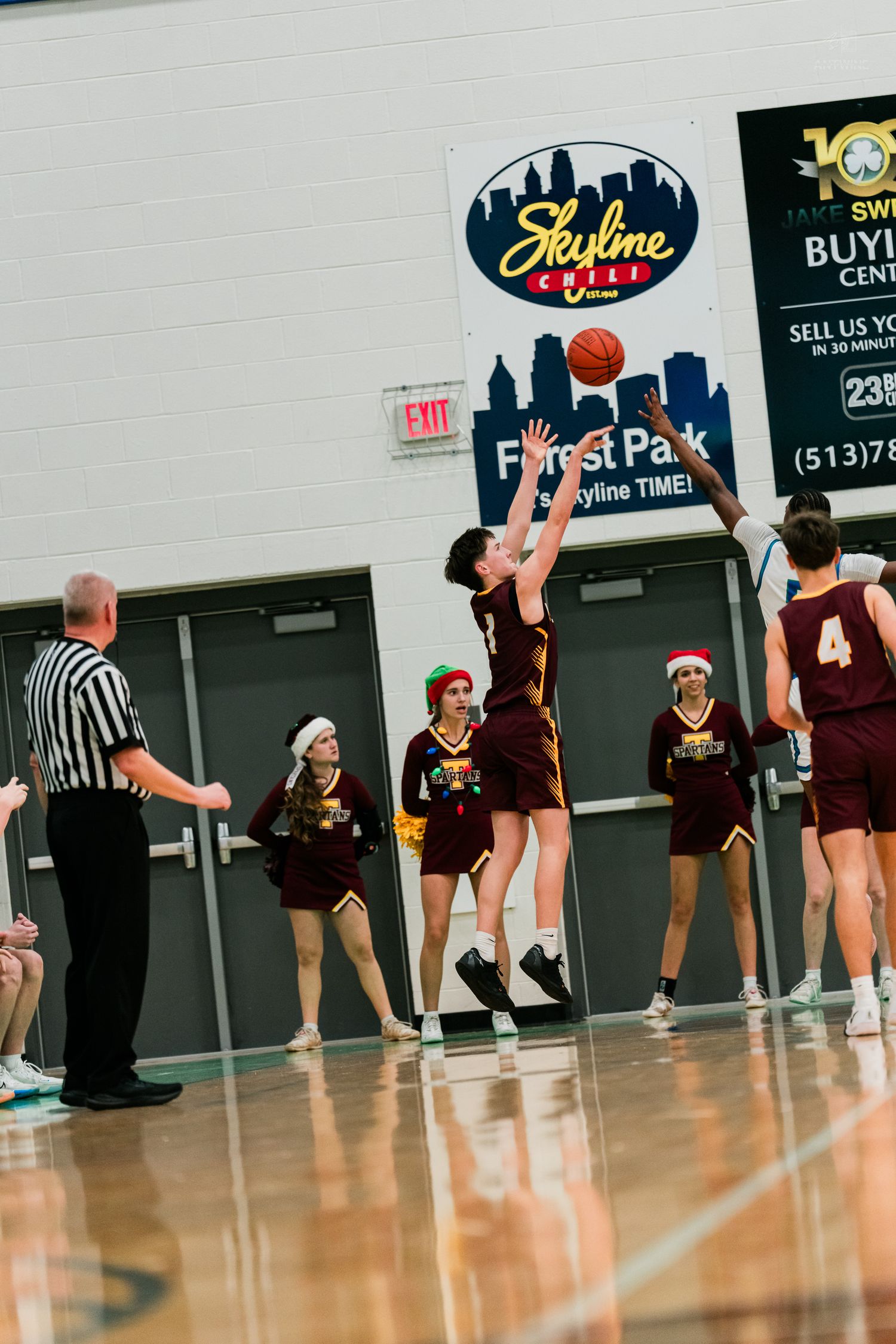 A Turpin basketball player shoots a jump shot near the basket as a referee and cheerleaders watch nearby.