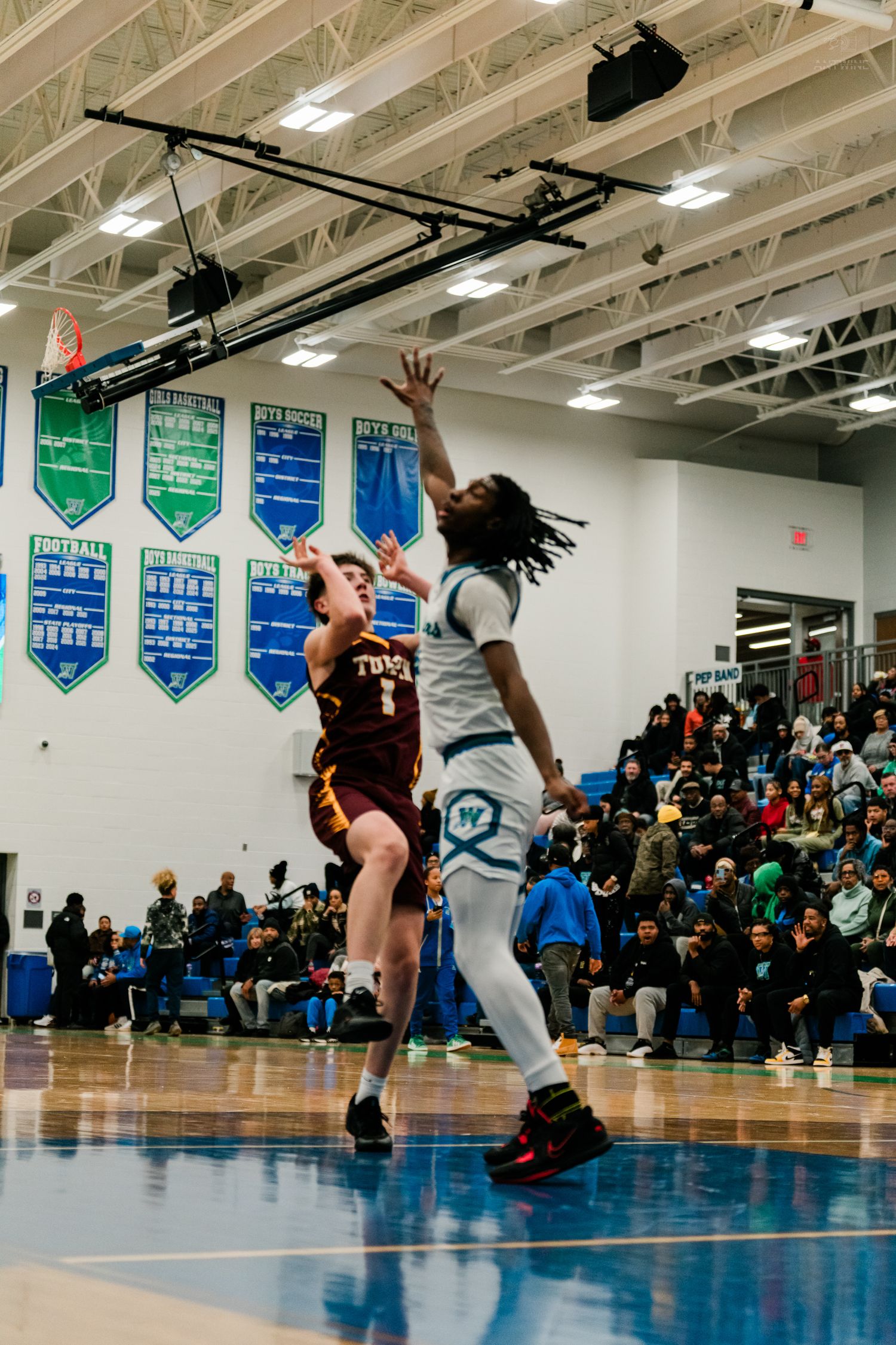 Turpin basketball player jumps to contest shot attempt by home team player in white uniform during packed gym game.