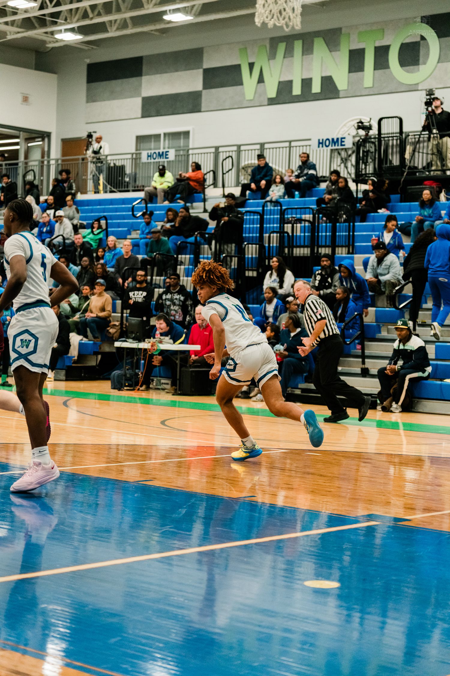 A Winton Woods player sprints down the court past a referee during a fast-paced high school basketball game.