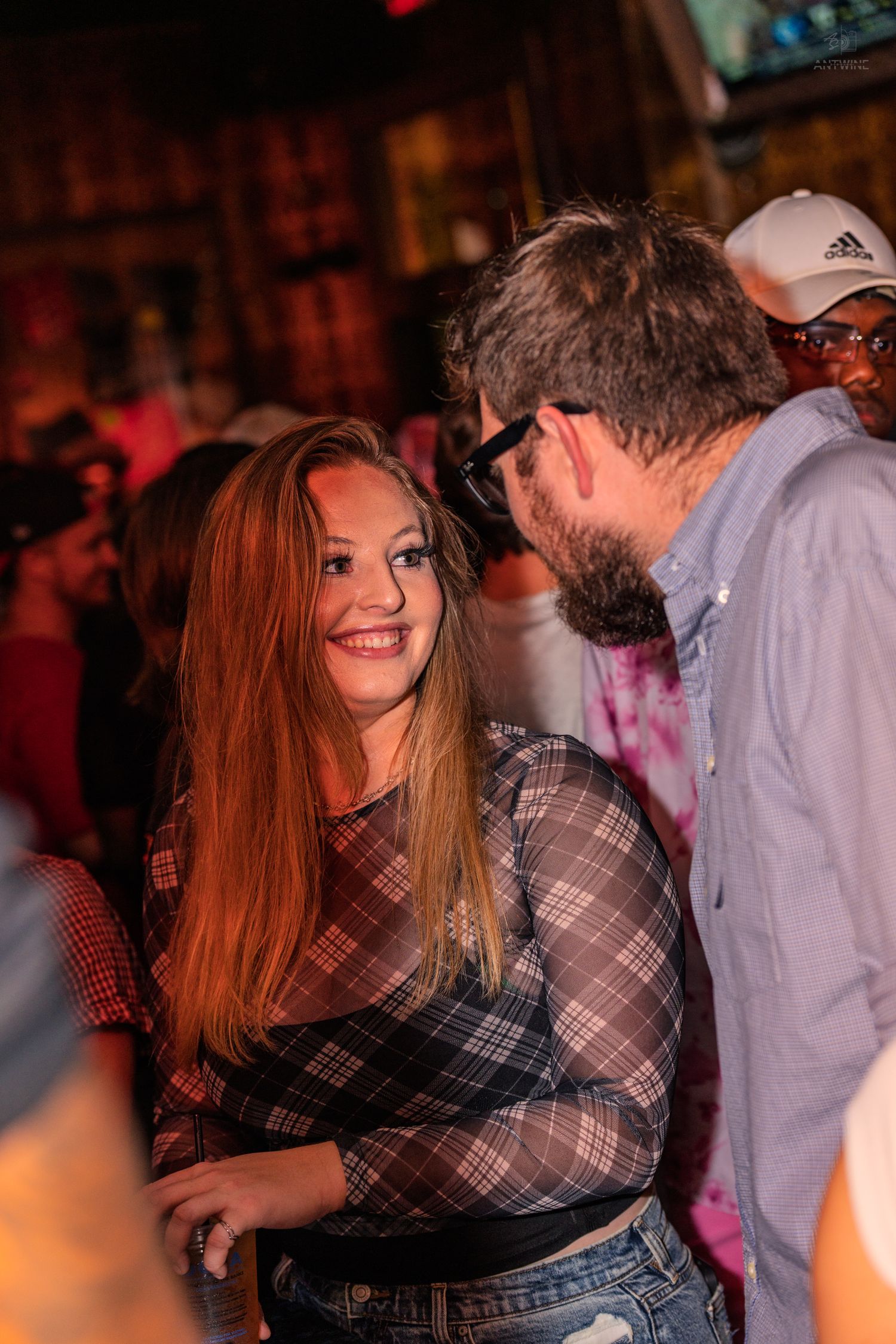 Young woman smiling at a bearded man wearing glasses at a crowded bar.