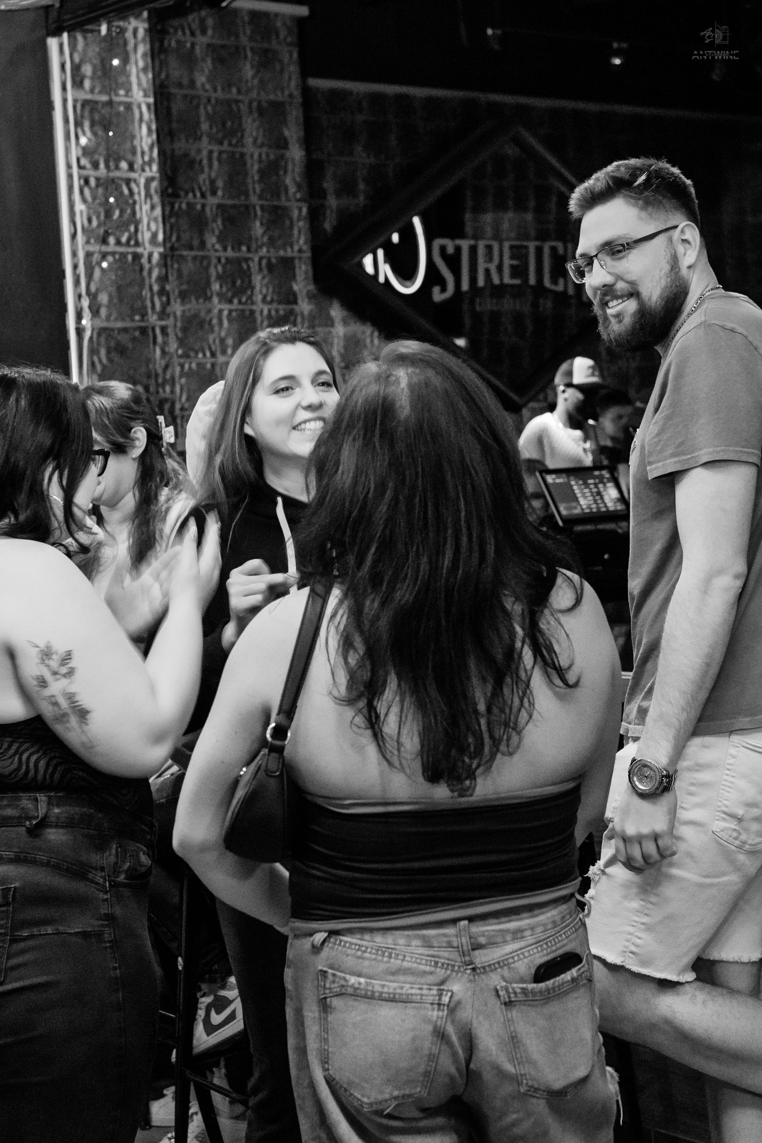 Black and white photo of a smiling group of friends socializing outside a bar with a Stretch sign.
