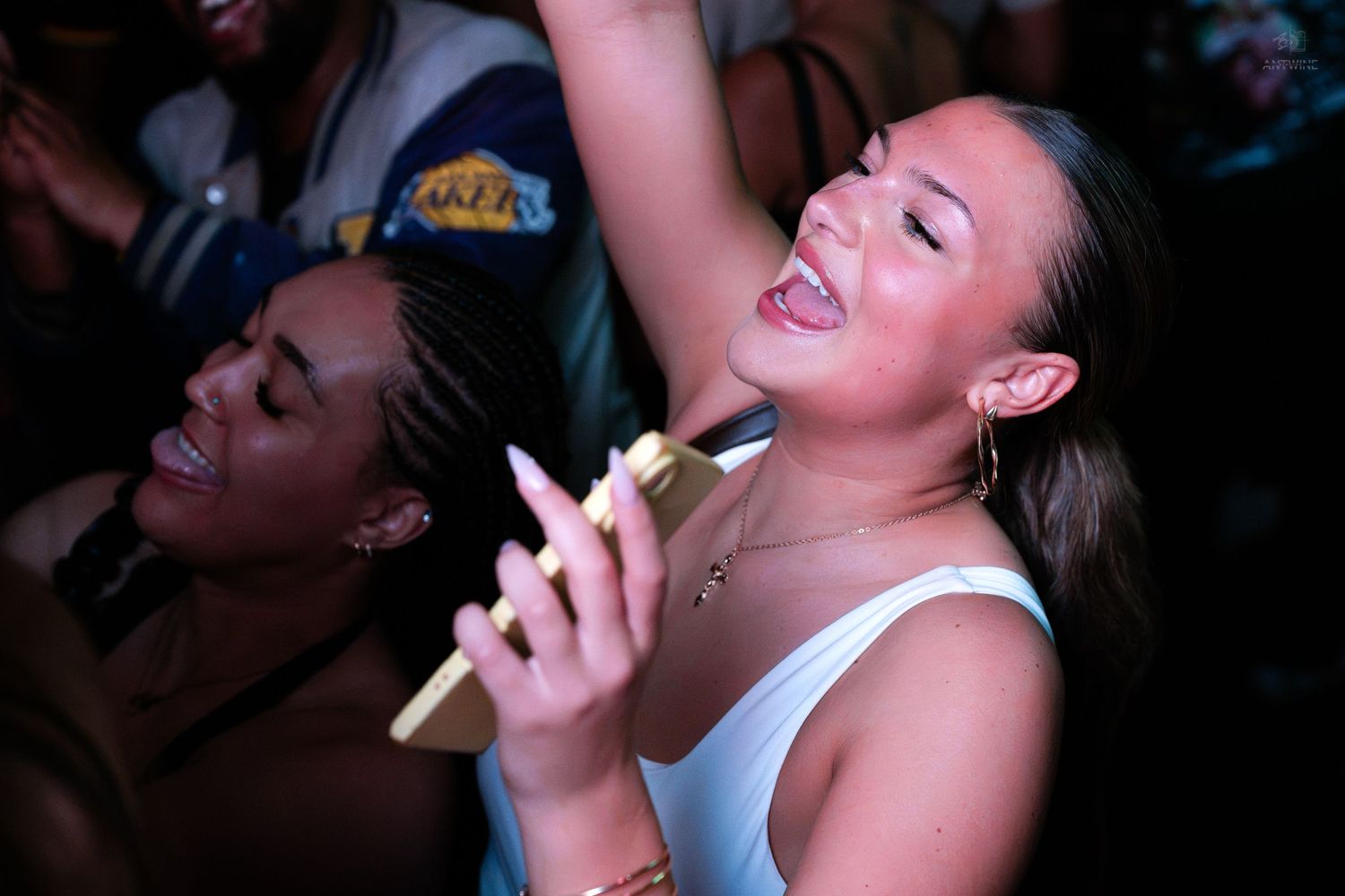 Excited young woman singing along holding a phone at a lively nightclub party.