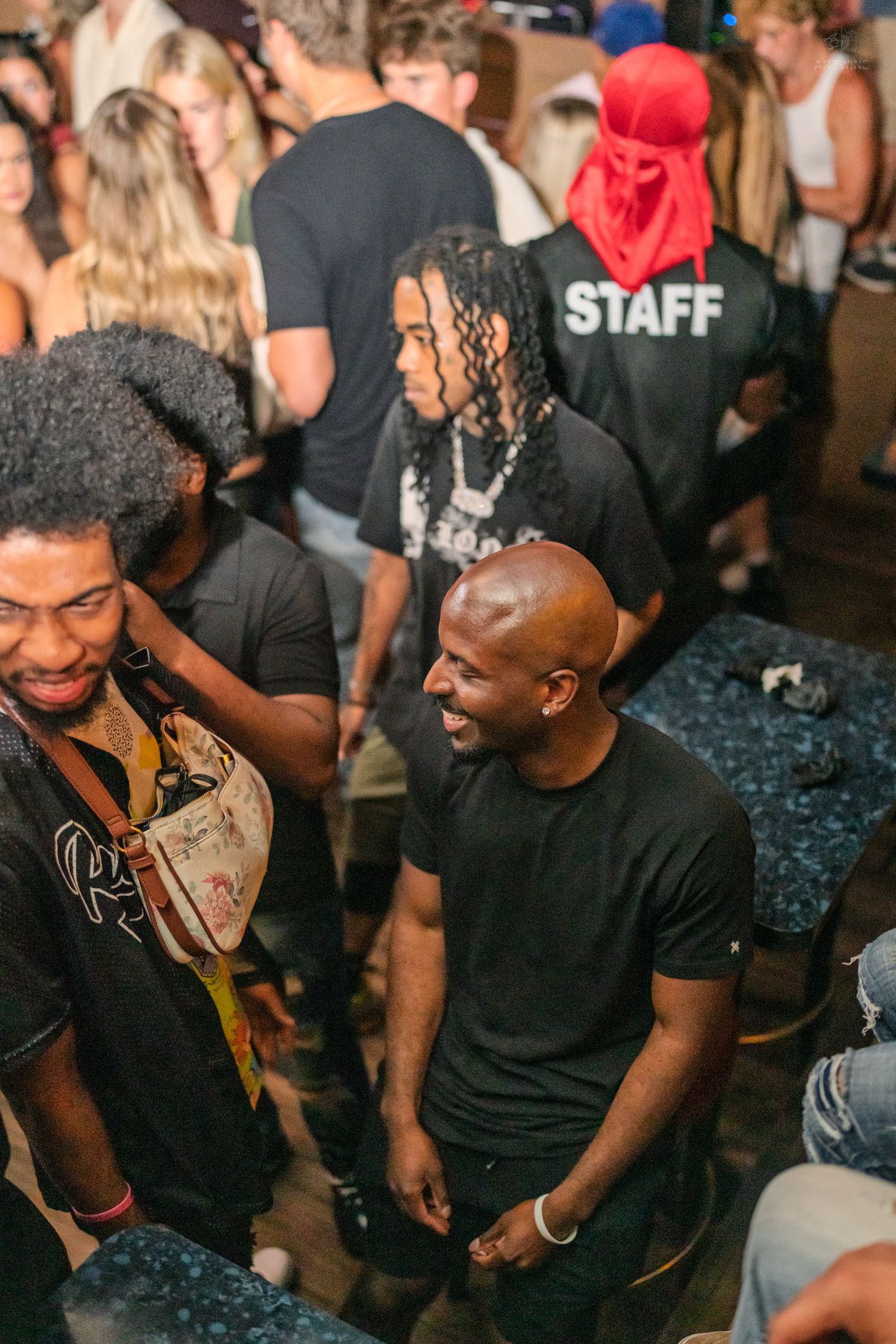 Men in black shirts socializing at a crowded nightclub with a staff member visible.