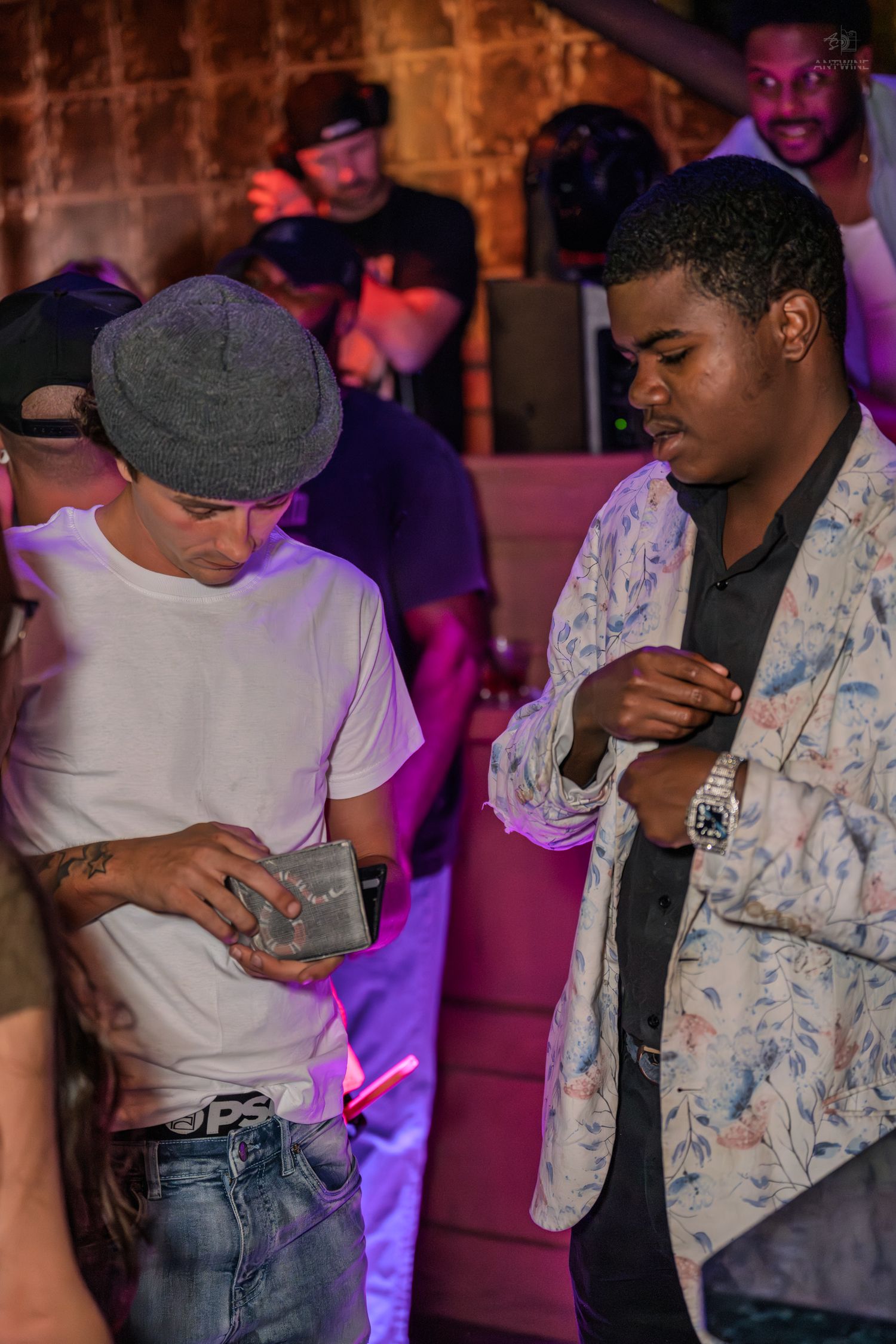 Two men examining an item under purple lights at a lively nightclub event.