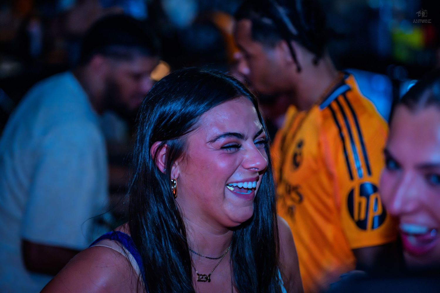 Laughing woman with dark hair at a lively bar event with friends nearby.